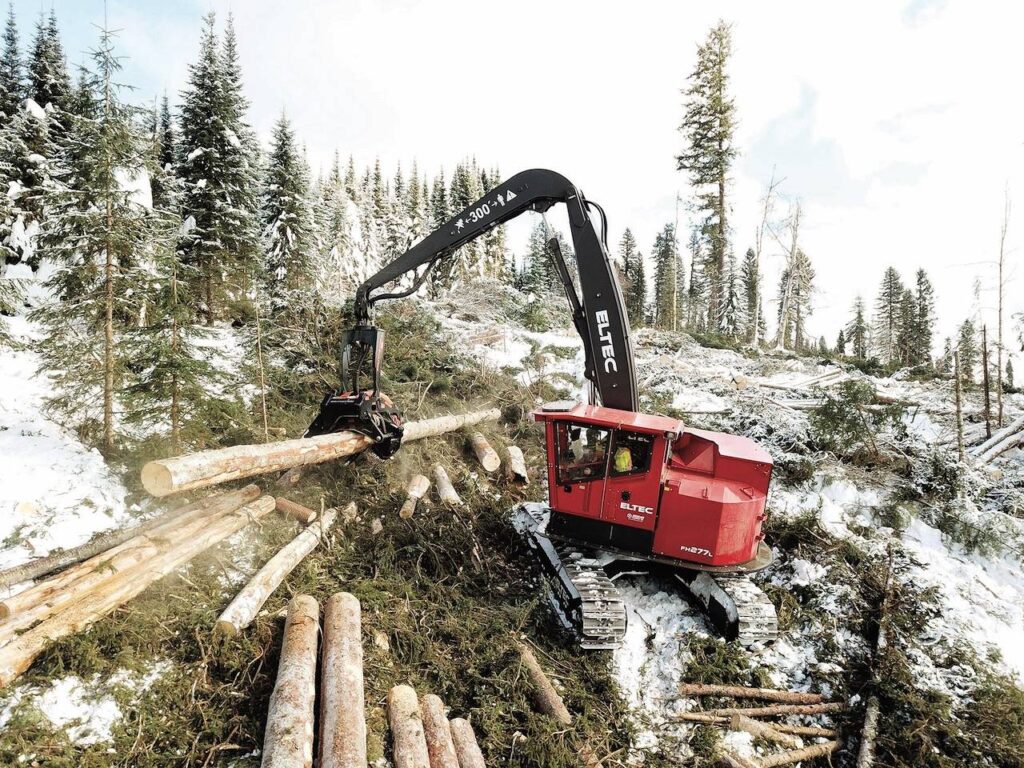 Eltel shovel loader in a snowy forest carrying logs on a job site.